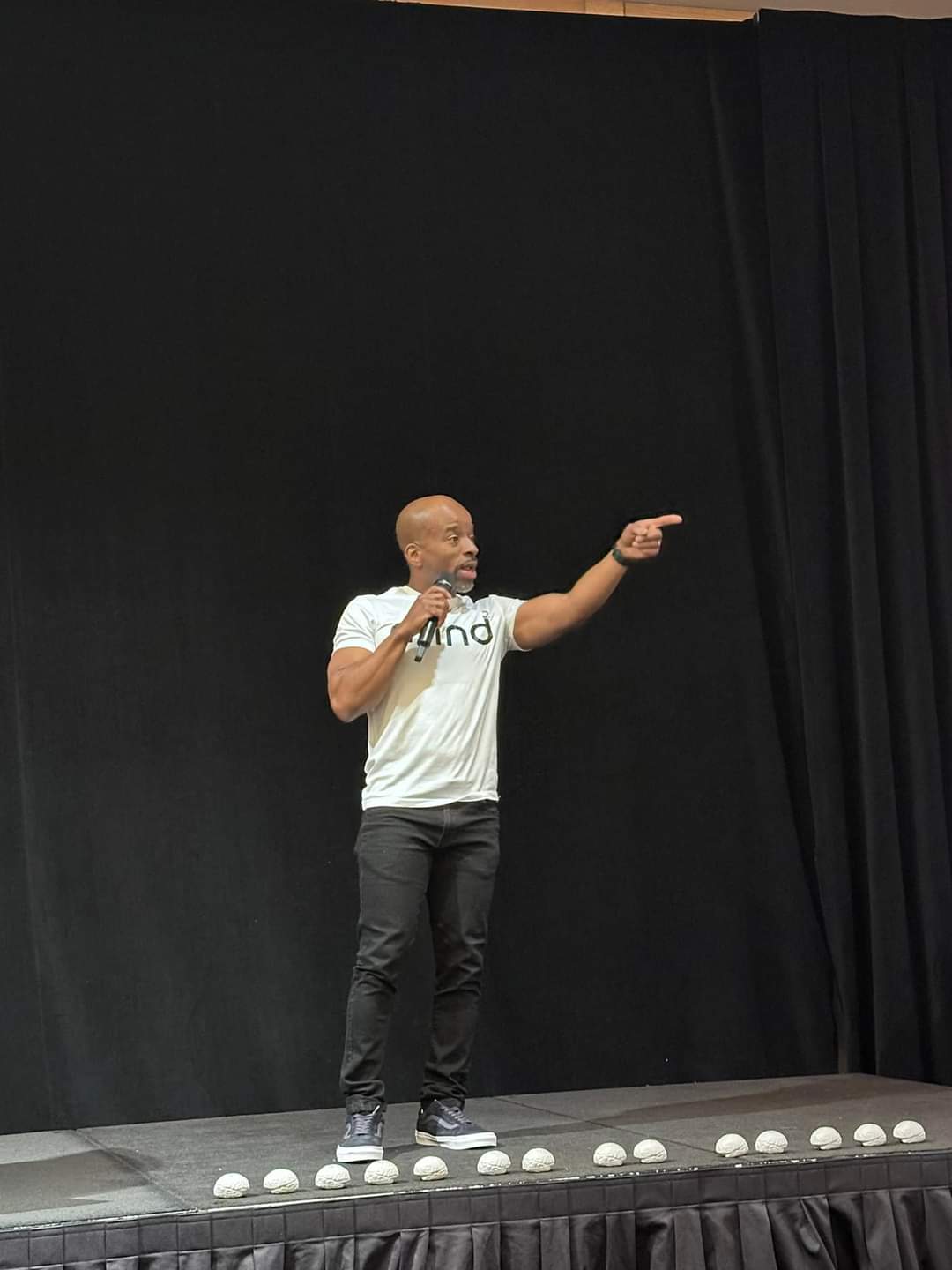 Tiko Blane speaking on stage, holding a microphone and pointing toward the audience